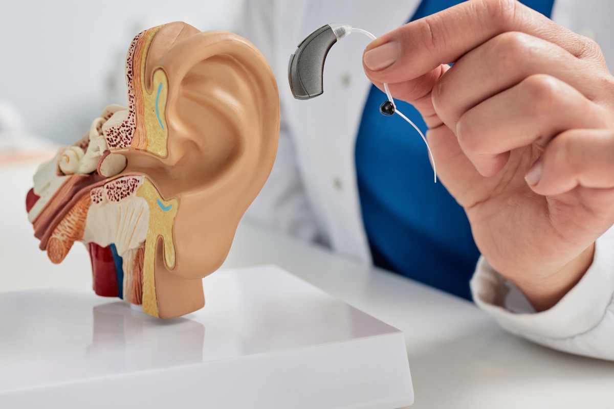 otorino mostra un orecchio e un apparecchio acustico