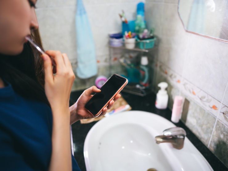 donna che usa smartphone mentre si lava i denti