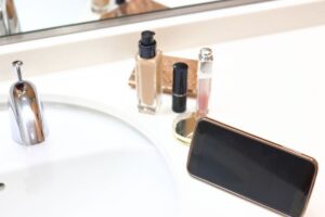 smartphone sul lavandino del bagno accanto a dei cosmetici